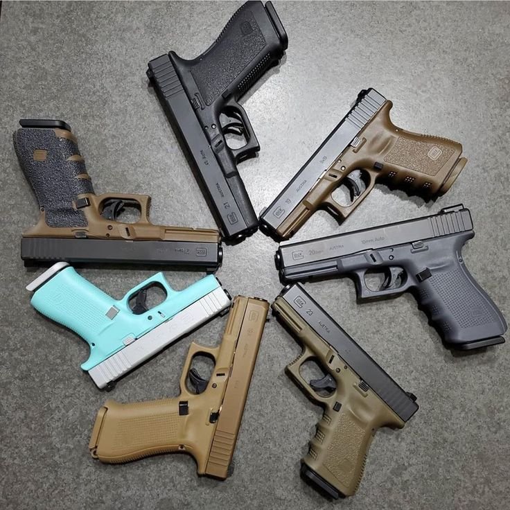 Collection of Glock pistols in various models and colors arranged in a circular pattern on a gray surface.