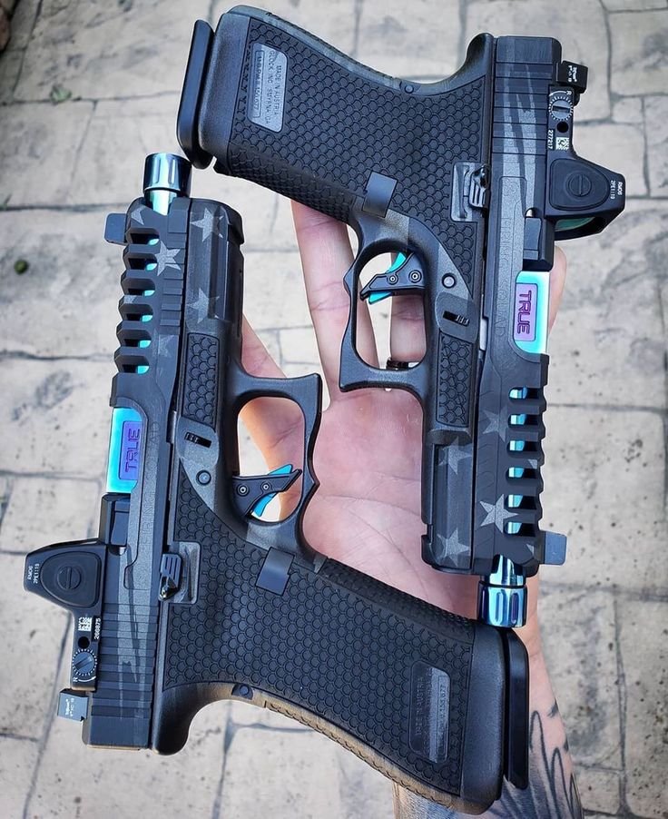 Two customized black pistols with blue and purple accents, held in one hand over a tiled surface.